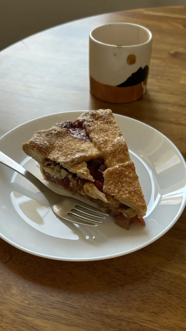 A piece of rubarb pie on a plate with a fork next to it and a little mug. 