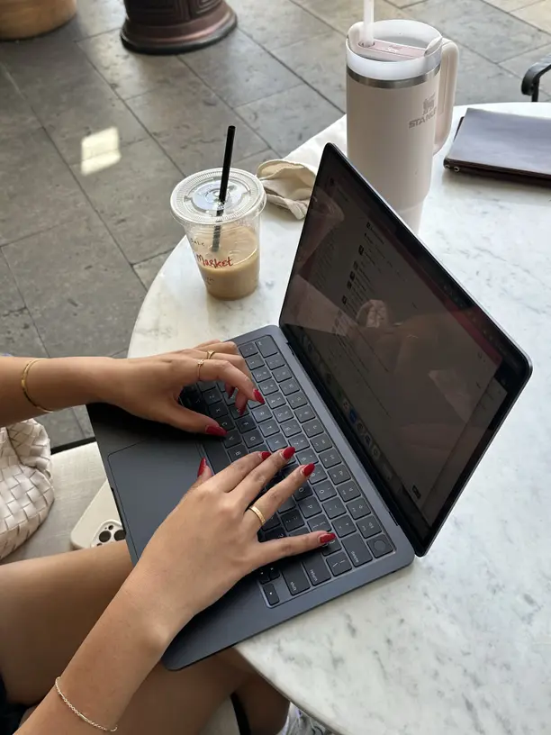 Creator working on a laptop at a cafe table, iced coffee beside her, building her newsletter and content plan